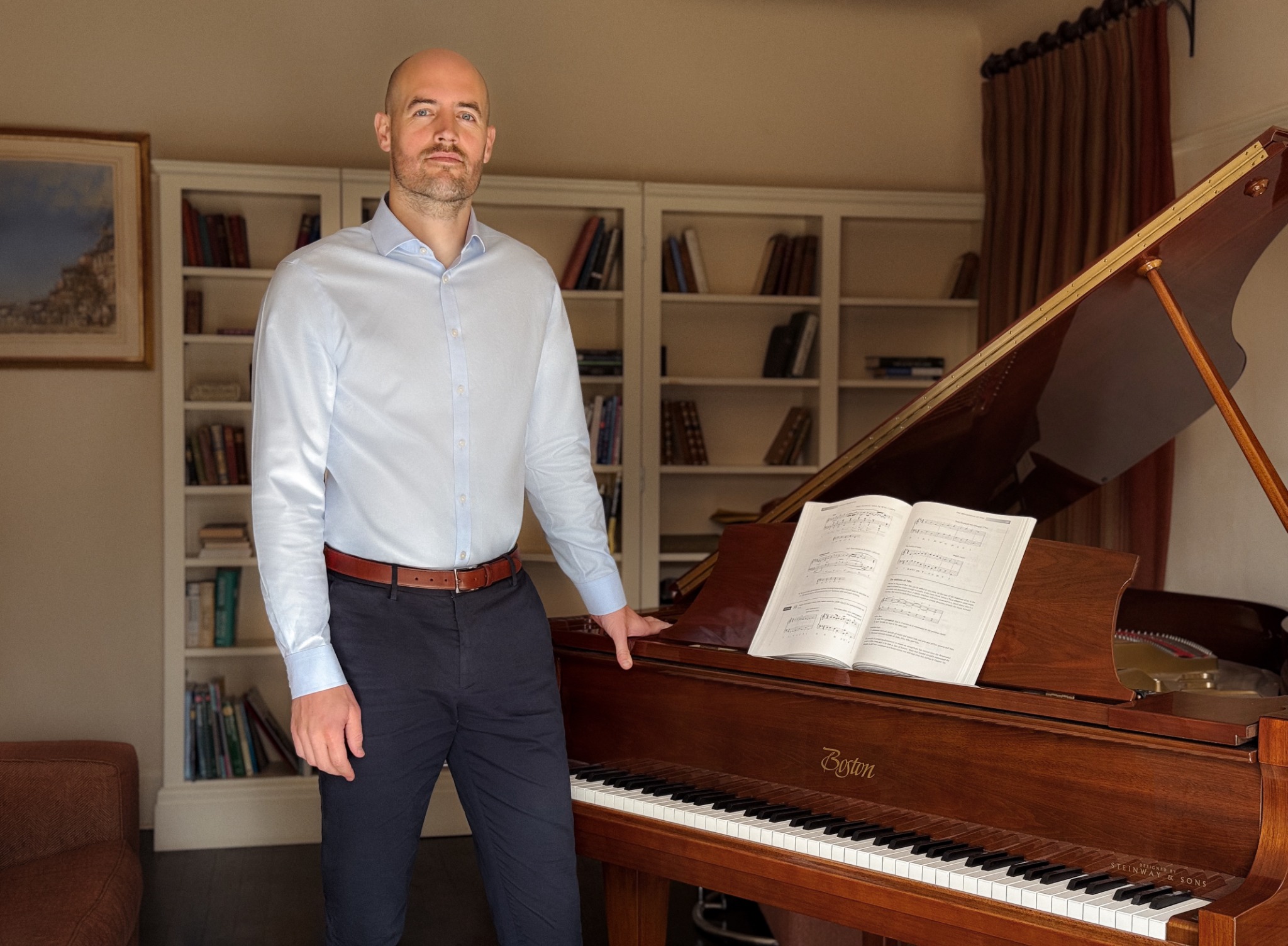 Phil Bennetts standing beside a Boston grand piano with an open score.